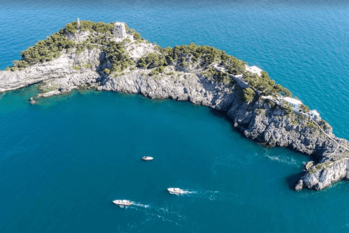Aerial view of rocky island with boats in blue sea.