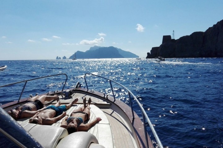 People sunbathing on a yacht with a scenic sea and mountain view.