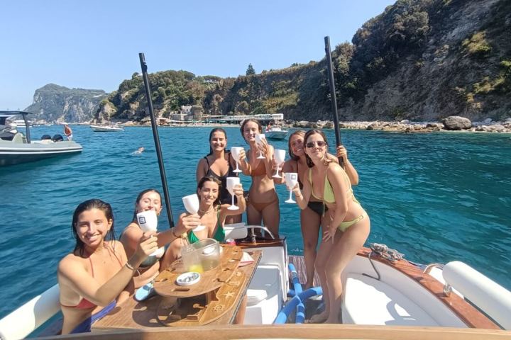 Group of women on a boat, enjoying drinks near a rocky coastline.