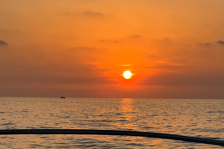 Sunset over calm sea with boats on horizon, viewed from a boat.