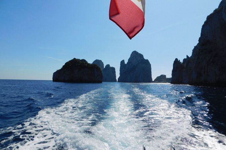 Boat trail on blue sea with rocky islands in distance under clear sky.