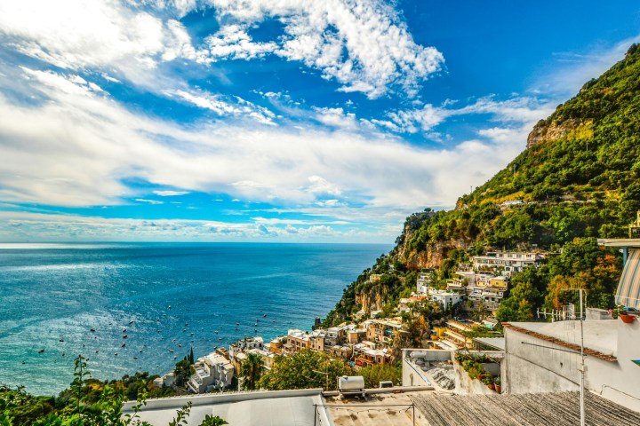 Coastal town with white buildings on a hillside overlooking the sea under a blue sky with clouds.