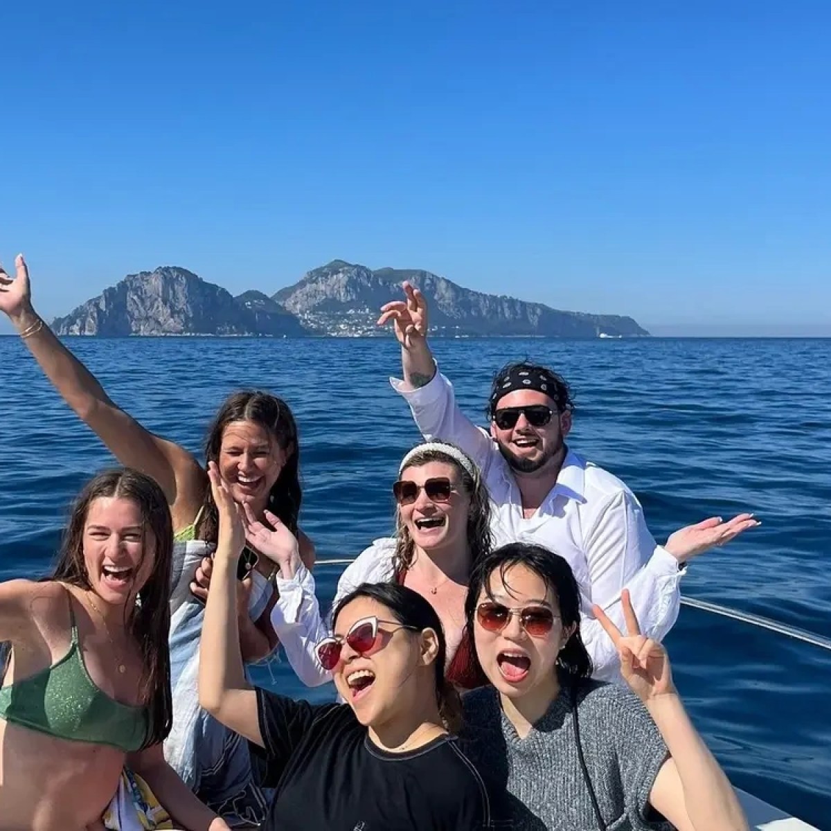 Group of people smiling on a boat with mountains in the background.