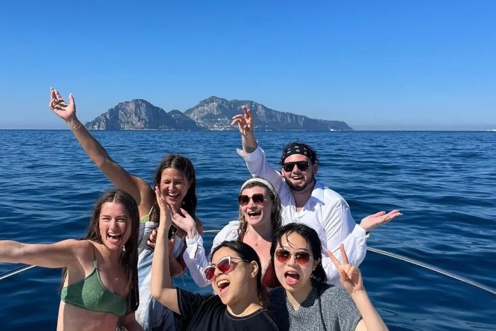 Group of people smiling on a boat with mountains in the background.