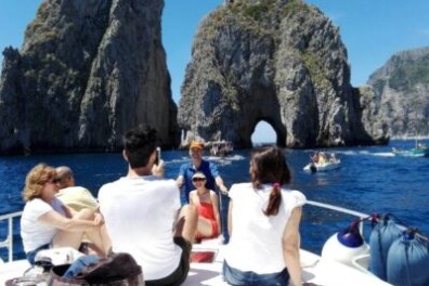 People on a boat near towering rock formations in the ocean under clear blue sky.