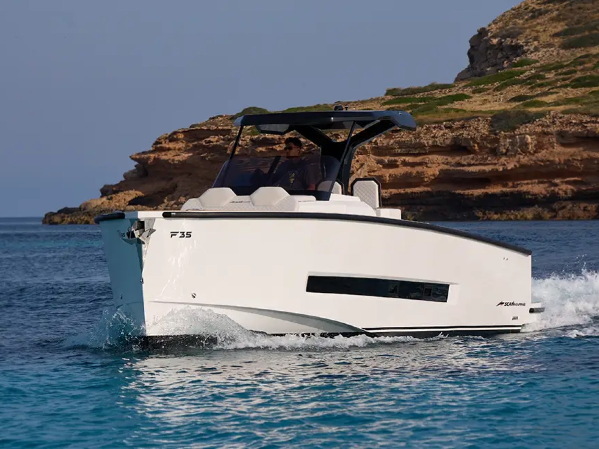Modern white motorboat cruising near a rocky coastline.