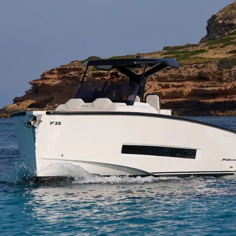 Modern white motorboat cruising near a rocky coastline.