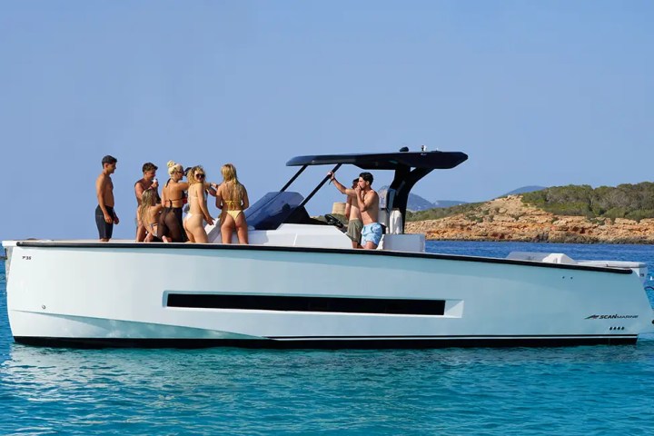 Group of people on a boat in clear blue water with rocky shoreline.