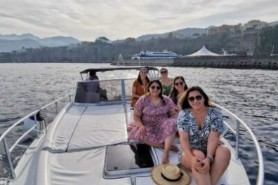Five people sitting on a boat with a scenic coastline in the background.