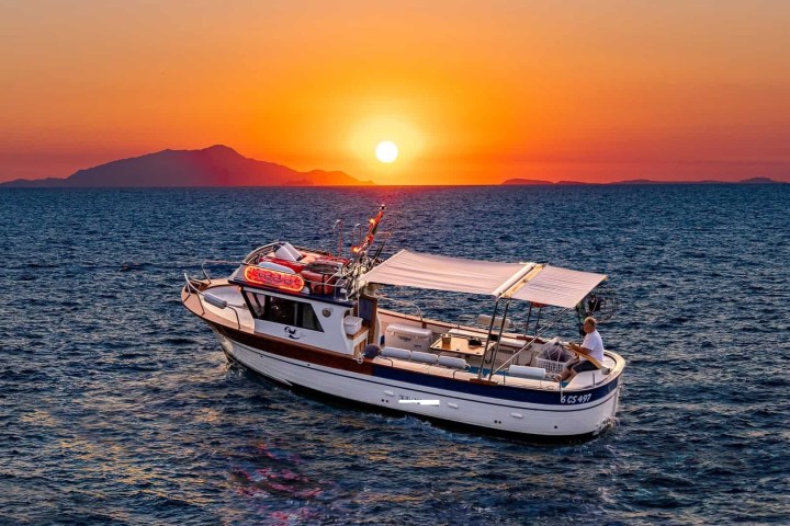 Boat on sea at sunset with island silhouette in background.