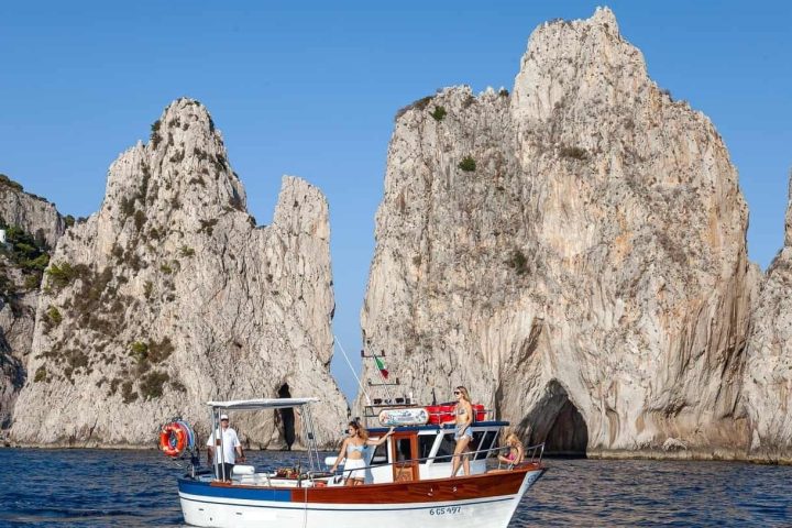 Boat on sea with people, rocky cliffs in background.