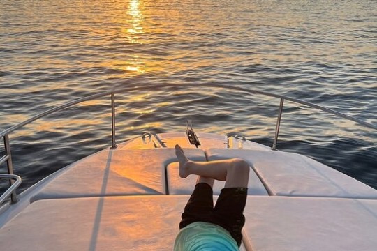 Person relaxing on a boat deck at sunset over calm ocean waters.