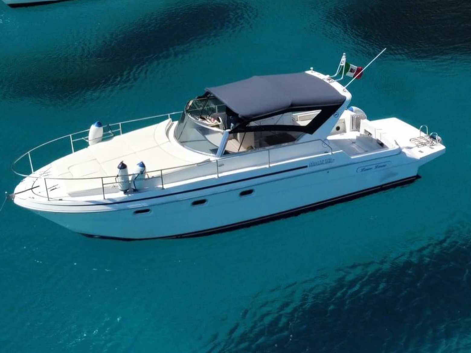 White motorboat with a dark canopy on clear blue water.