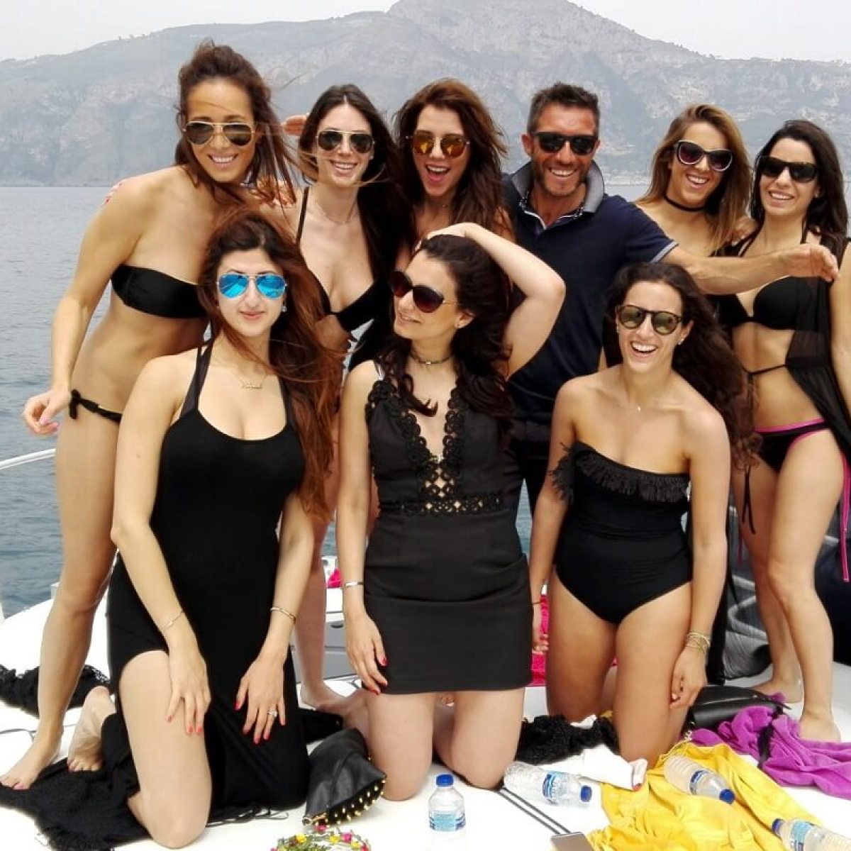 Group of people in swimwear on a boat with mountains in the background.