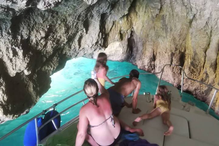 Four people on a boat inside a rocky cave with turquoise water.