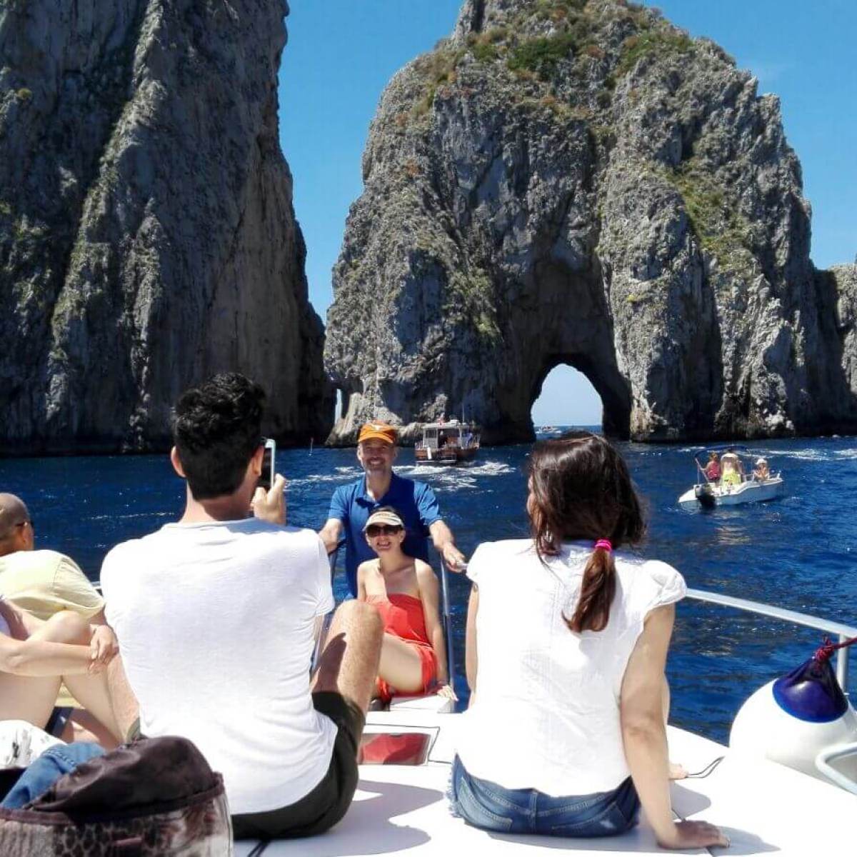 People on a boat near large sea rock formations under clear blue sky.