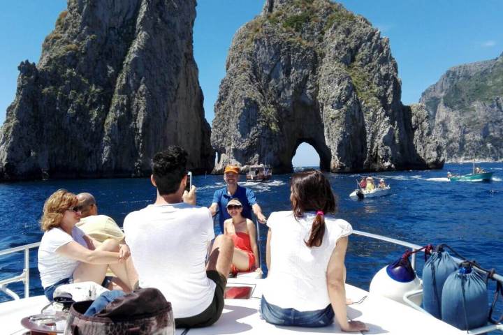 People on a boat near rocky cliffs and blue sea on a sunny day.