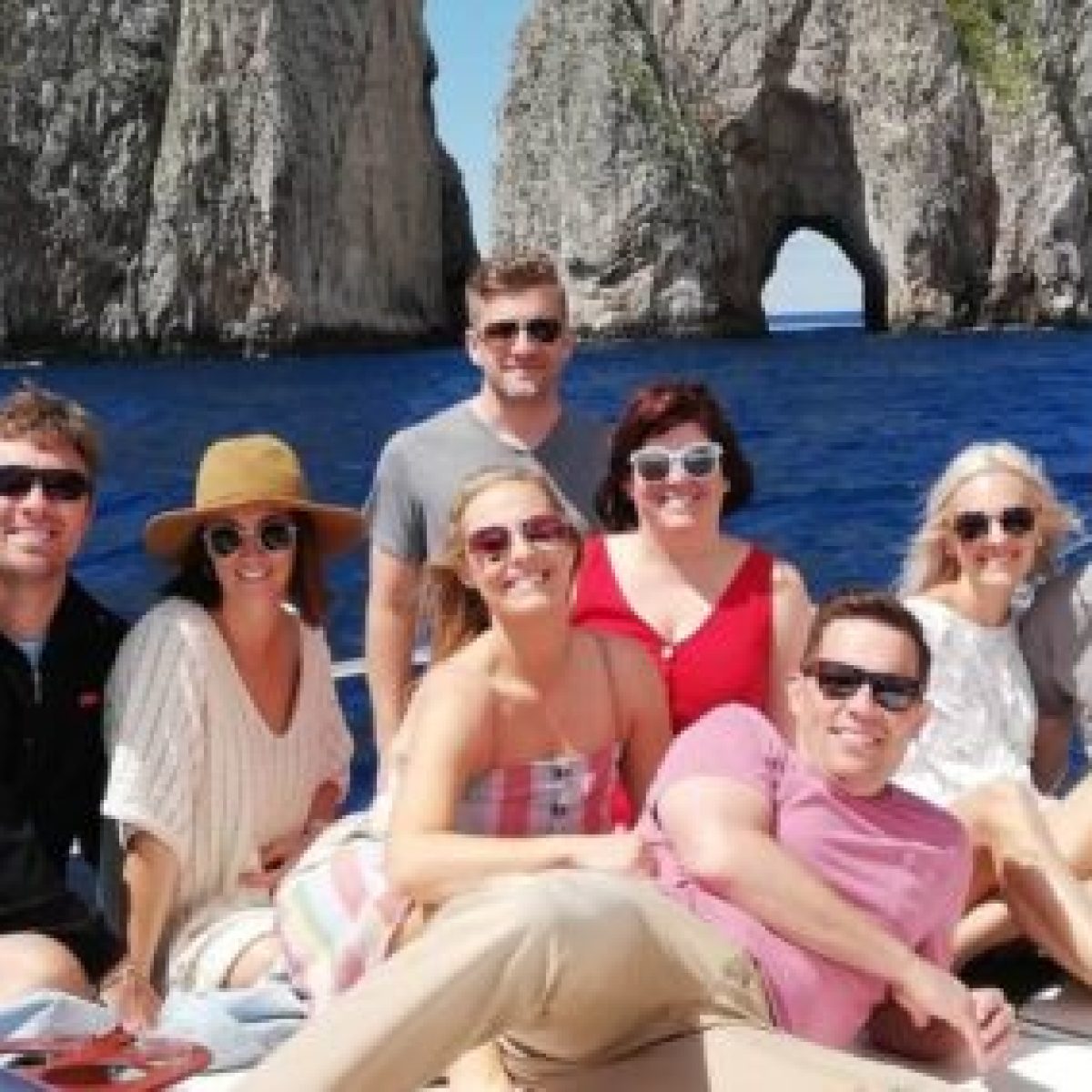 Group of people smiling on a boat with rocky cliffs in the background.