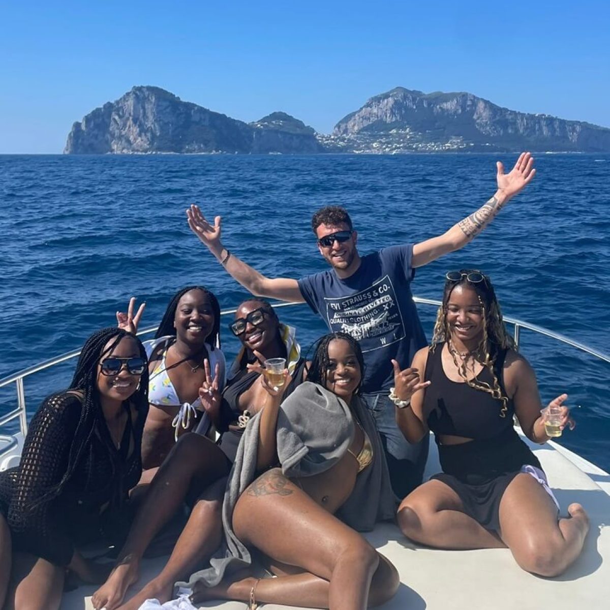 Group of friends posing on a boat with rocky islands in the background.