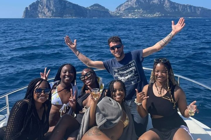 Group of friends posing on a boat with rocky islands in the background.