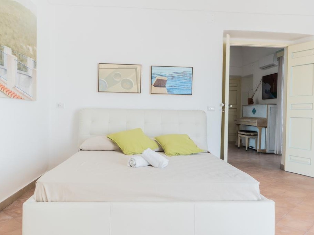 Bedroom with white bed, green pillows, art on walls, open door.