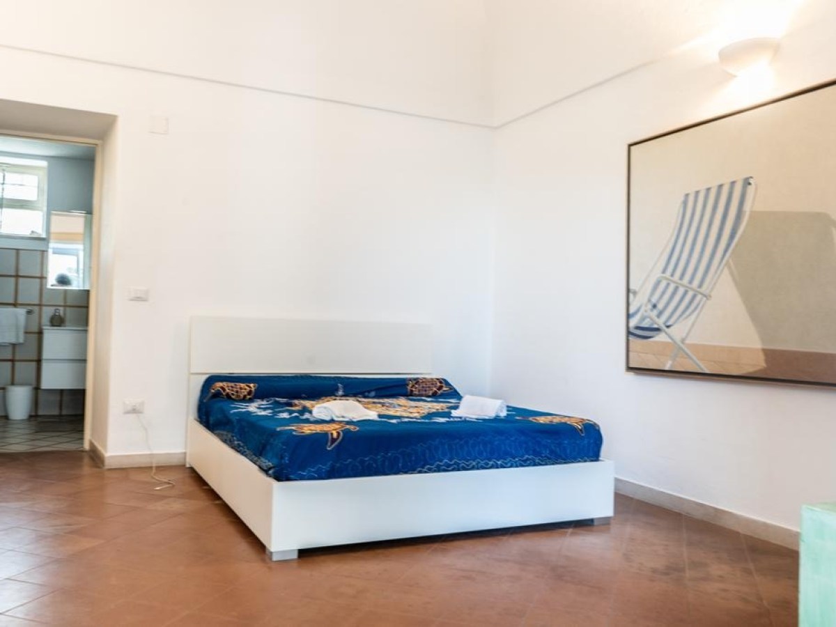 Minimalist bedroom with blue bedspread, wall art, and open door to tiled bathroom.