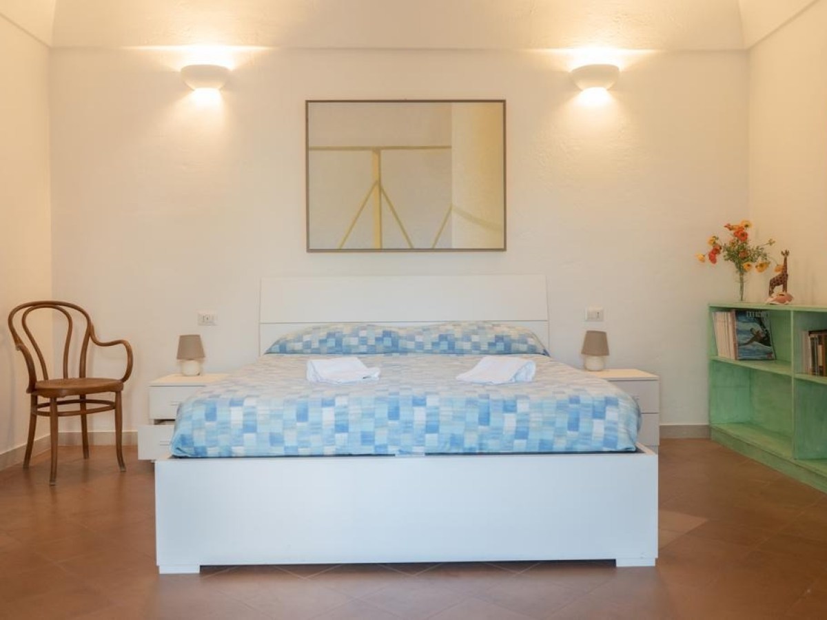 Minimalist bedroom with a double bed, chair, and bookshelf.