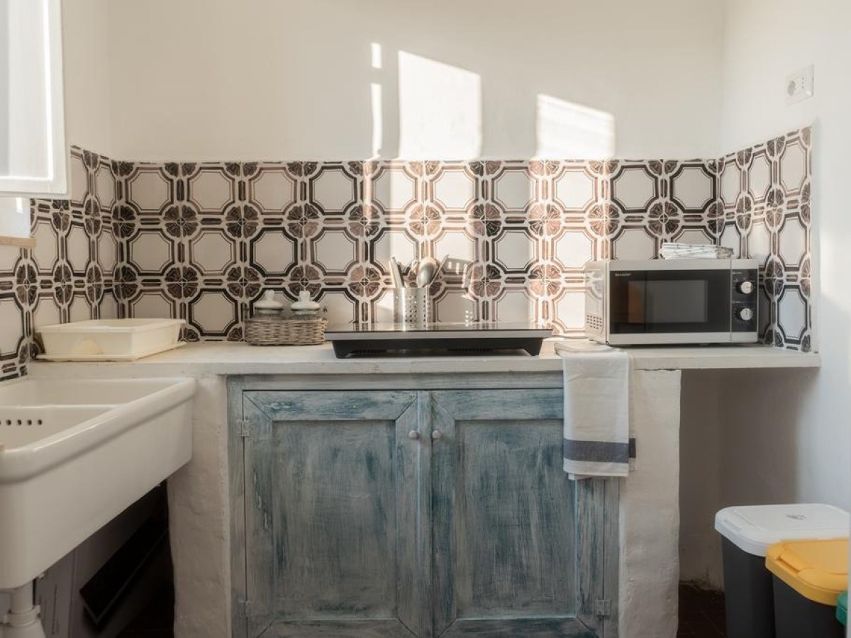 Cozy kitchen with vintage tile backsplash, sink, microwave, and cabinet.