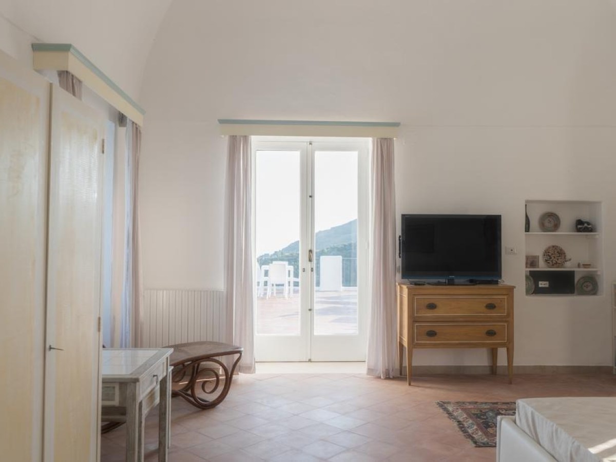 Bright room with TV on wooden dresser, door leading to patio with sea view.