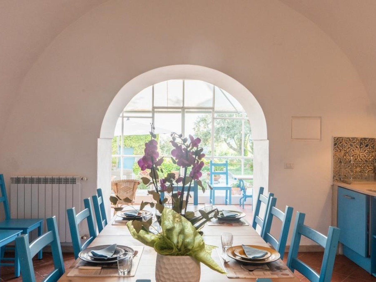 Dining room with blue chairs, set table, and flowers by arched window.