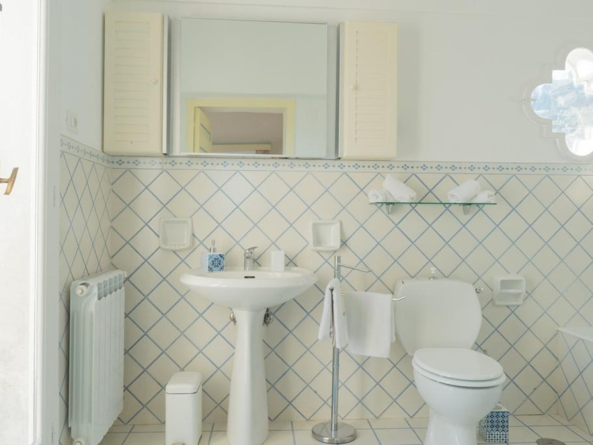 White bathroom with tiled walls, pedestal sink, toilet, and mirror.