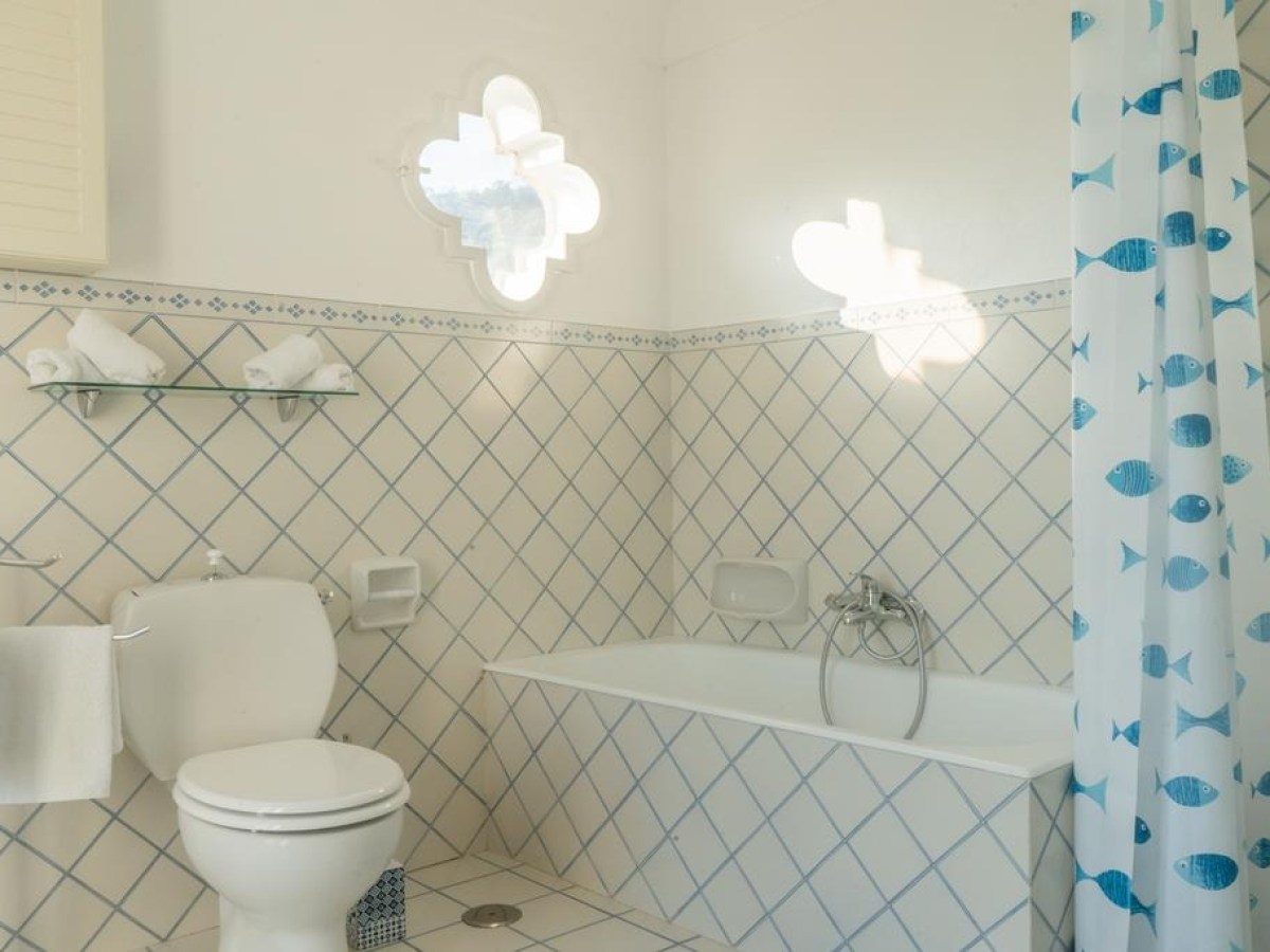 Bright bathroom with a fish-themed shower curtain, bathtub, and white tiles.