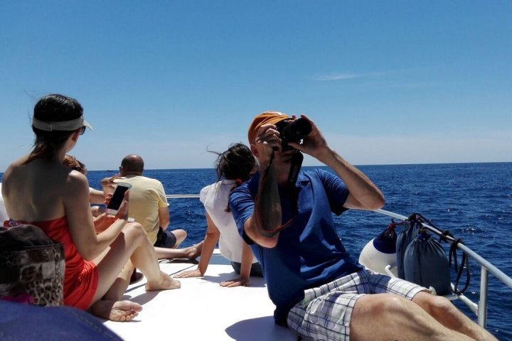 People sitting on a boat, one using binoculars, with the ocean in the background.