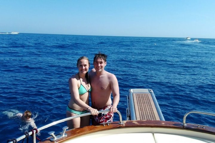 Two people in swimwear on a boat with the sea in the background.