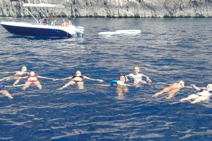 Group of people floating in the sea near a boat, holding hands.